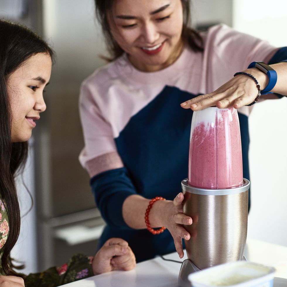 woman pressing down on juicing machine as daughter watches