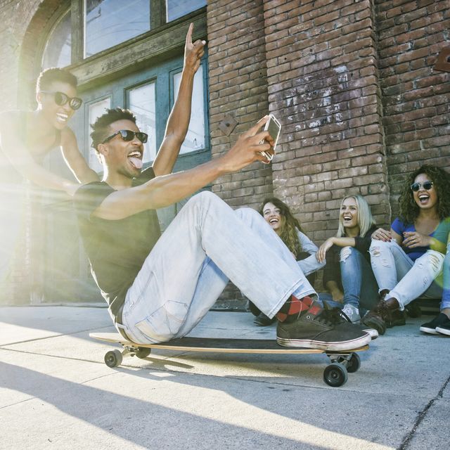 Woman pushing friend sitting on skateboard in city
