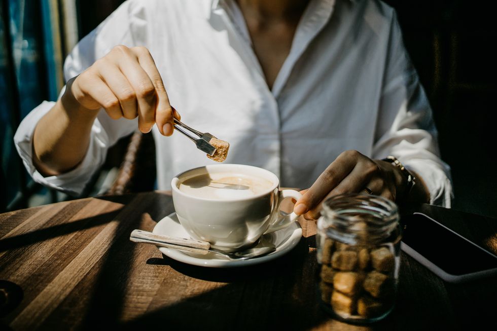woman putting brown sugar cube into coffee and ready to enjoy it on a fresh morning