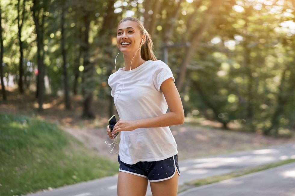 woman putting on earphones to listen music before jogging summer park