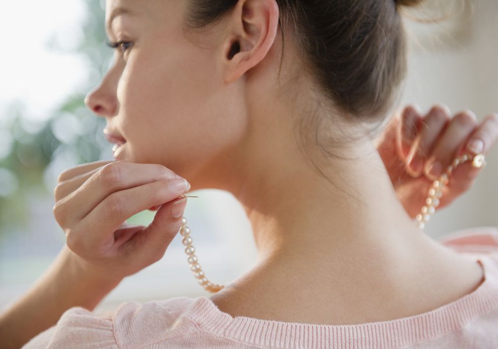 woman putting on pearl necklace