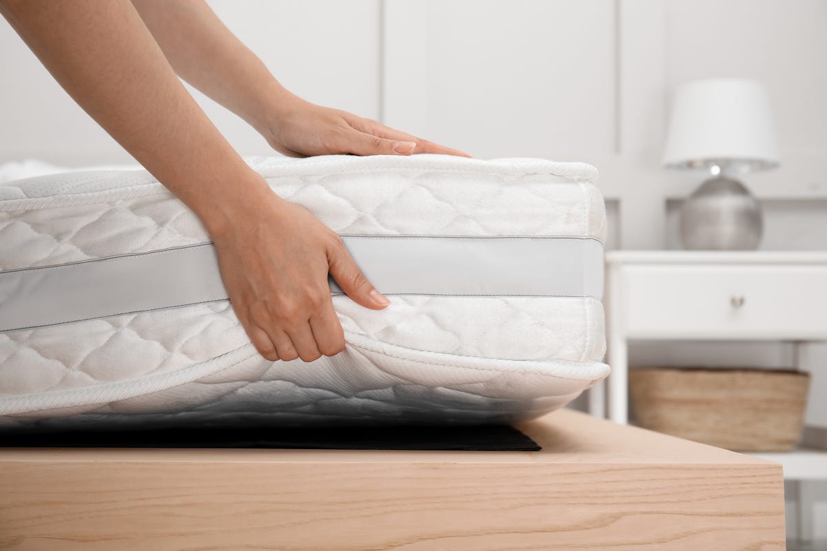 woman putting soft white mattress on bed indoors, closeup