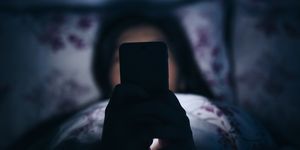 woman reading and texting on smartphone in bed