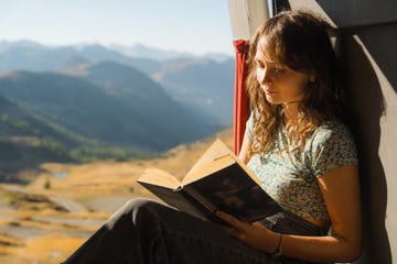 woman reading book in camper van in mountains