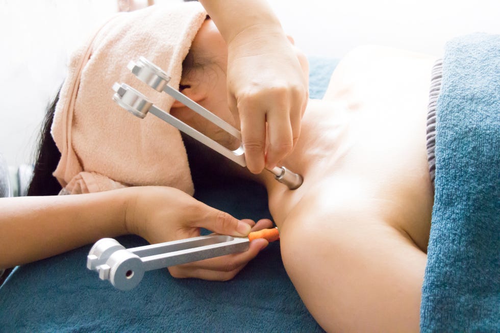 mujer recibiendo un tratamiento de belleza de sonoterapia con un diapasón