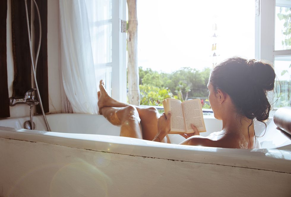 woman relaxing in bathtub reading book