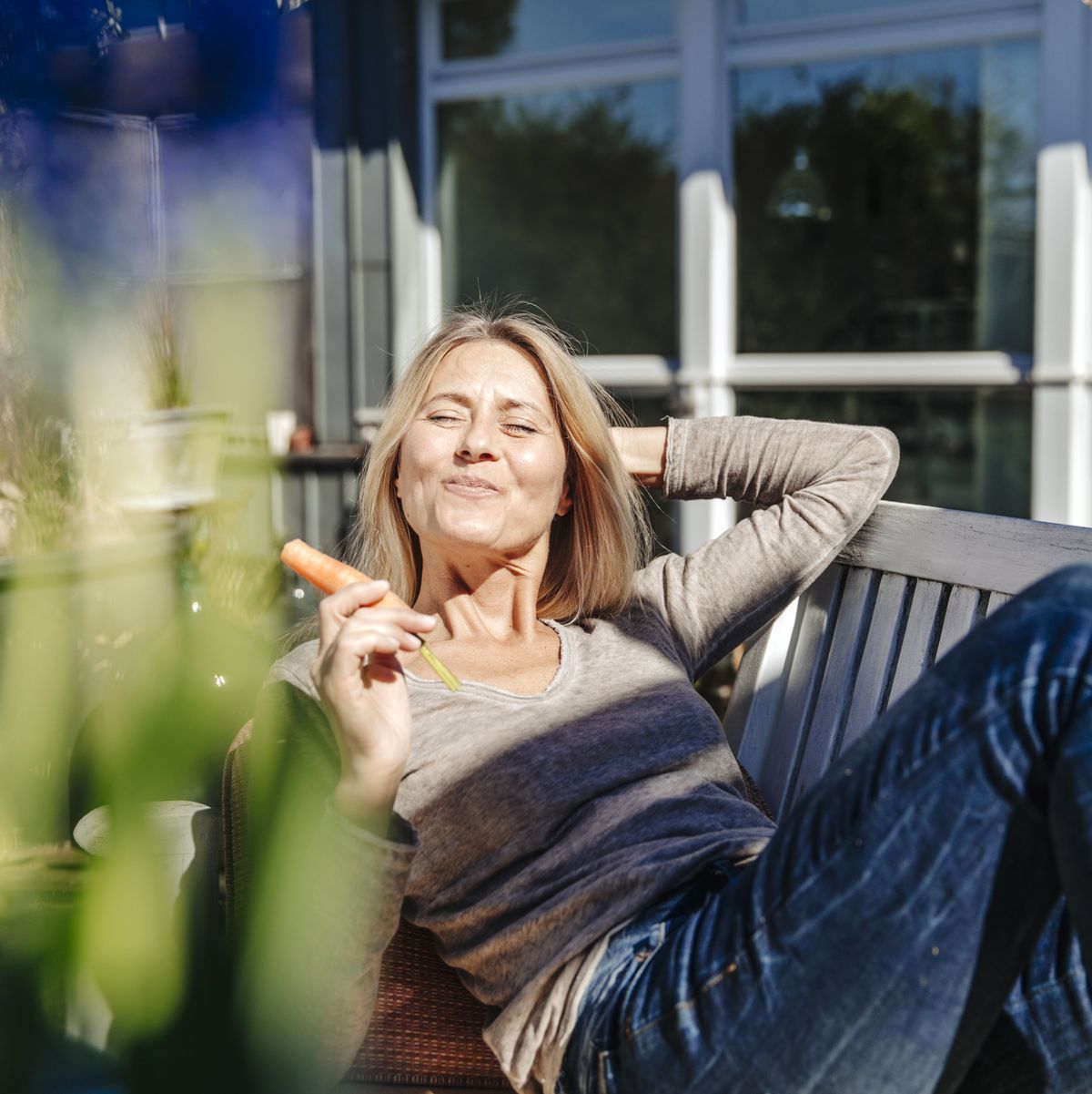 woman relaxing on garden bench eating a carrot