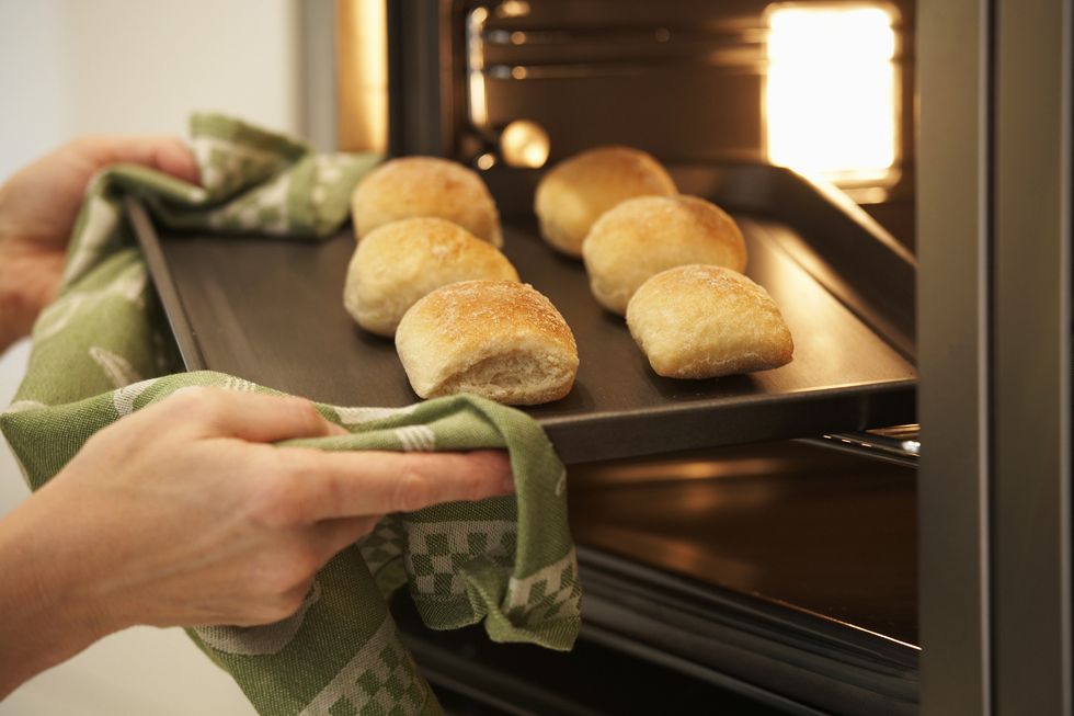 woman removing fresh baked breadcakes from an oven