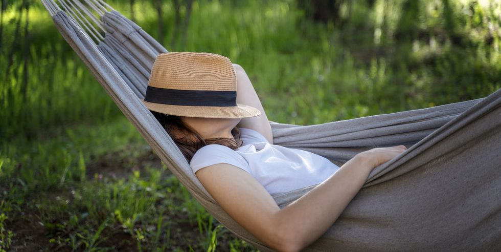 woman resting in a hammock in a summer garden covering her face with a straw hat summer relax vacation