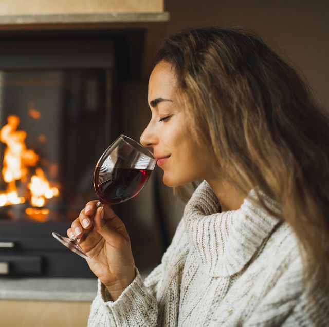 woman resting in evening and drinking red wine at home near fireplace autumn mood