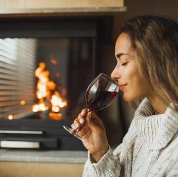 woman resting in evening and drinking red wine at home near fireplace autumn mood