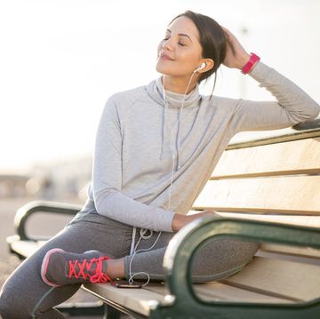 een vrouw zit op een bankje in haar sportkleding tevreden en rustgevend met haar ogen gesloten te genieten