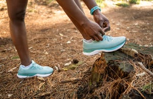 woman runner tying her shoelaces before going for a run on forest trail