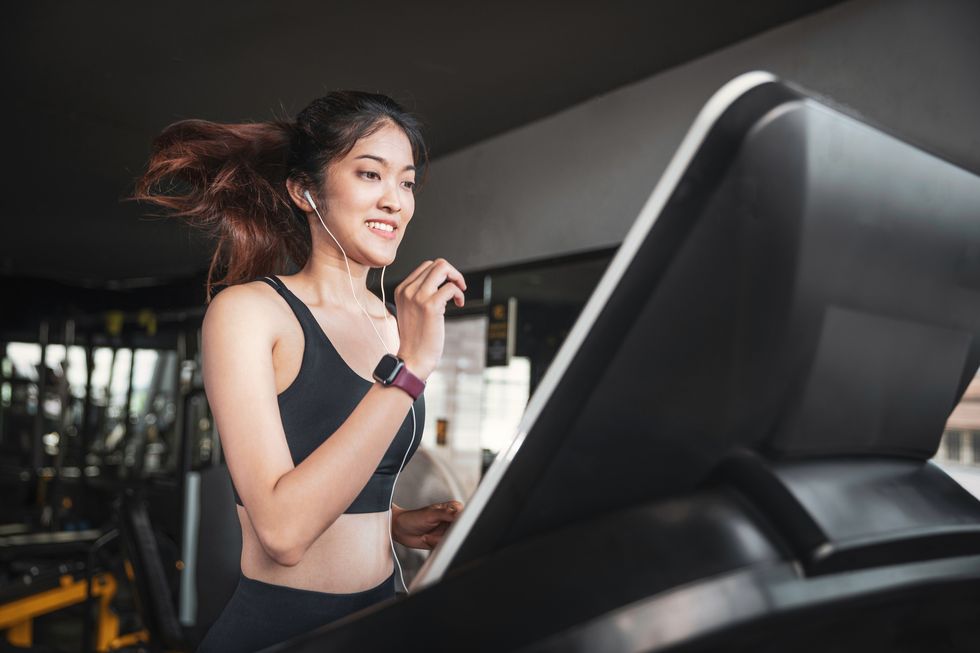 woman running in a gym on a treadmill concept for exercising fitness and healthy lifestyle girl running on the treadmill and listening to music at the gym