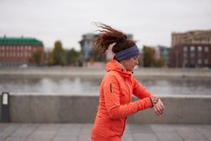 woman running in city street and checking pulse on watch