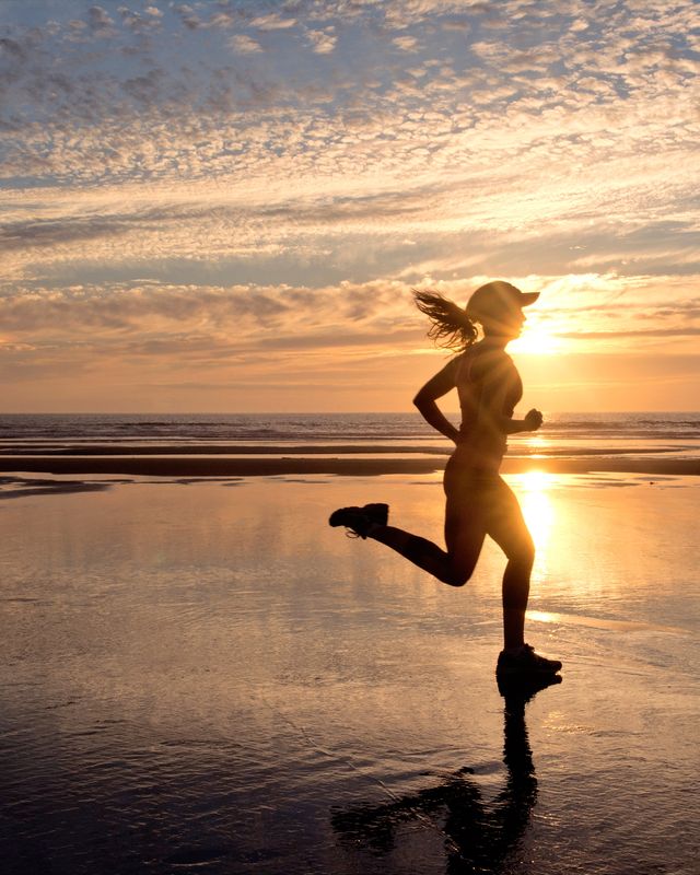 Woman running garvalin on beach at sunrise