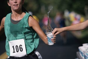 woman running road race, grabbing cup of water, mid section