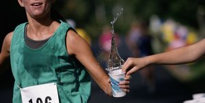 woman running road race, grabbing cup of water, mid section