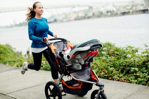 Woman running with baby stroller on footpath by river in city