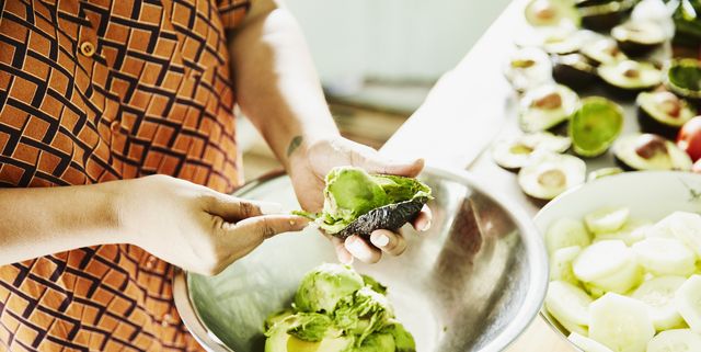 Woman scooping avocado into bowl while preparing food for party in kitchen
