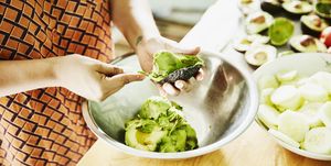 Woman scooping avocado into bowl while preparing food for party in kitchen