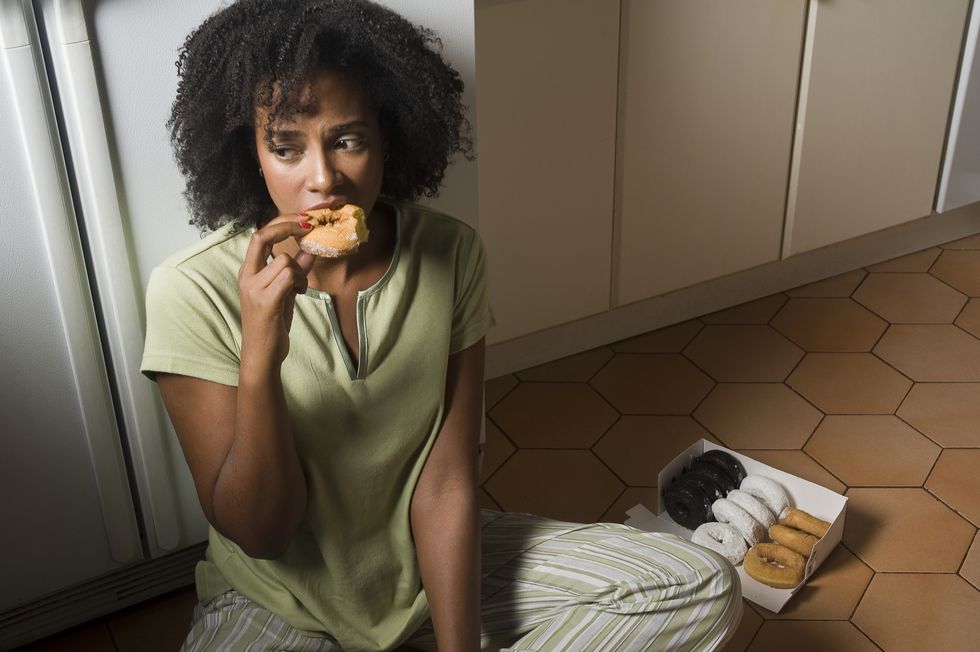 woman seated on kitchen floor at night eating doug