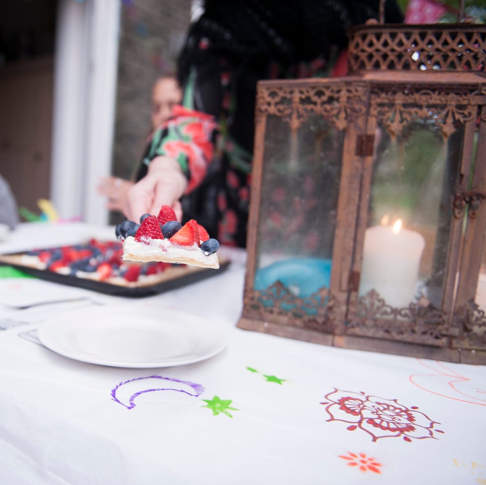 thanksgiving traditions – Woman serving fruit pie at a birthday party a woman's hand serving fruit tart over a white tablecloth with marker drawn colorful symbols on it