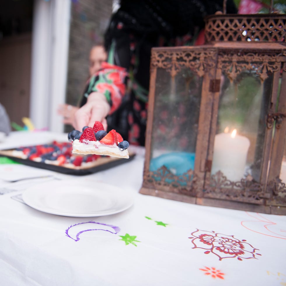 a woman's hand serving fruit tart over a white tablecloth with marker drawn colorful symbols on it