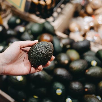 woman shopping for fresh fruit and vegetables in supermarket, close up of her hand choosing avocados
