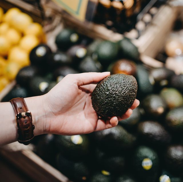woman shopping for fresh fruit and vegetables in supermarket, close up of her hand choosing avocados