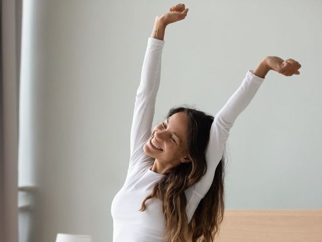 woman sitting in bed stretching her arms muscles after sleep