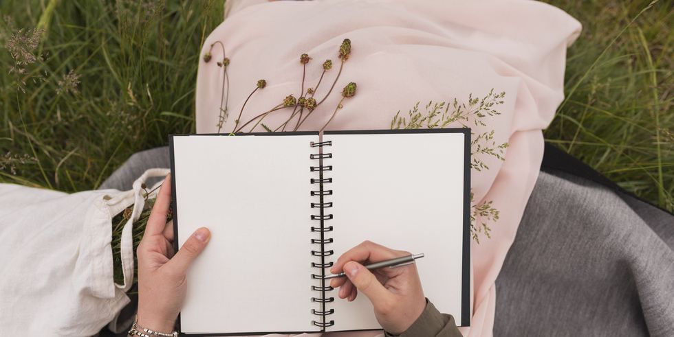 woman sitting on a meadow writing down something in her notebook, partial view