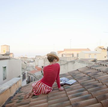 woman sitting on a tiled roof, reading cookbook