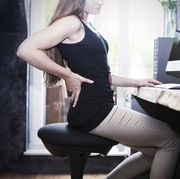 Woman sitting on health chair at desk holding her back
