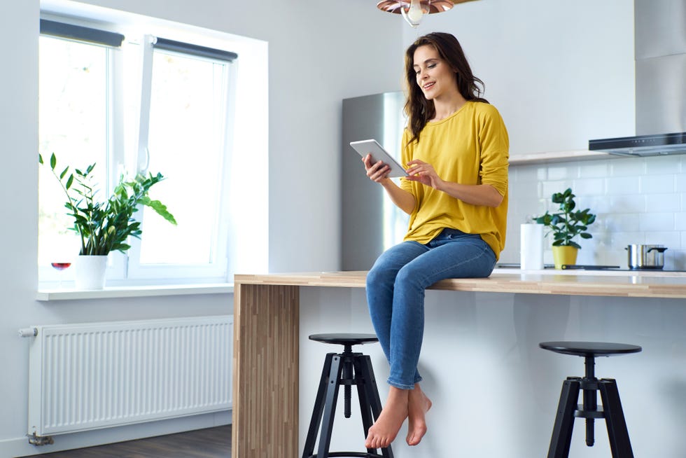 Woman sitting on kitchen counter at home, using digital tablet