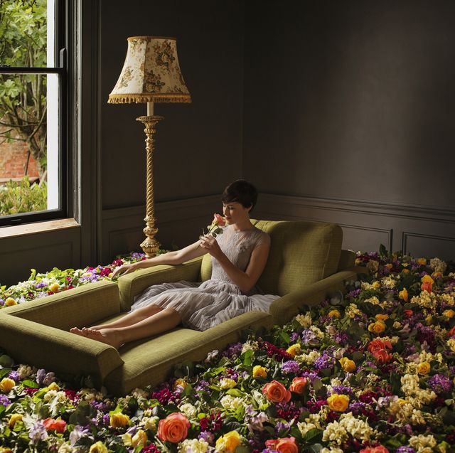 woman sitting on sofa surrounded by flowers