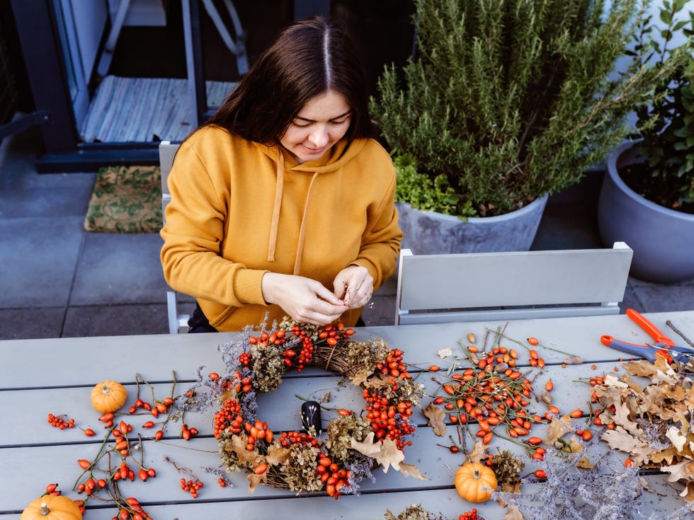 a woman making a fall wreath at a table outside
