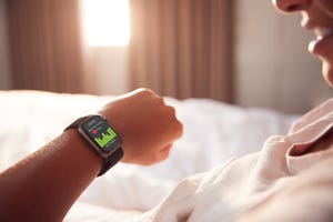 woman sitting up in bed looking at screen of smart watch