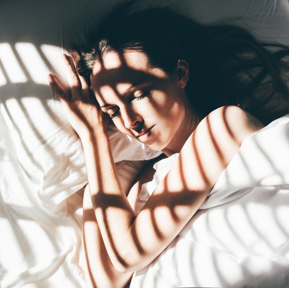 young woman sleeps in a comfortable bed sunbeam of dawn on her face