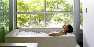 woman soaking in bubble bath, surrounded by glass windows, side view