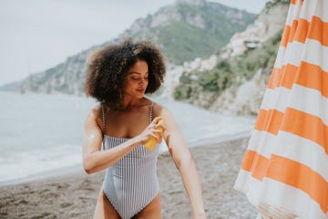 a woman spritzes her arm with spray sun screen at the beach