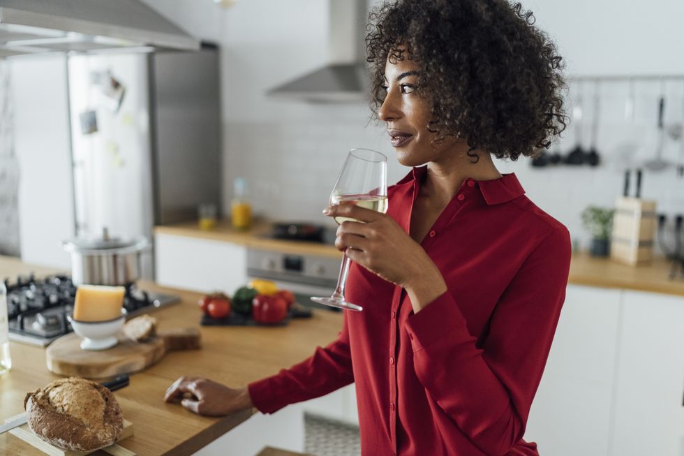 woman standing in kitchen, drinking a glass of white wine