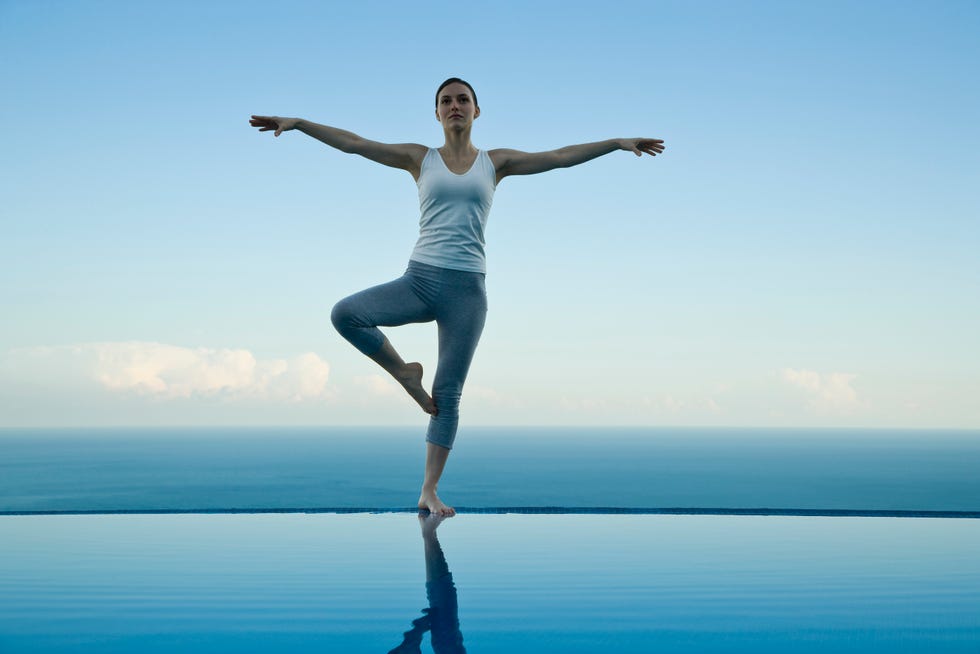 woman standing in tree pose on edge of infinity pool