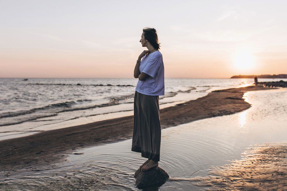 woman standing on the beach at sunset looking at view
