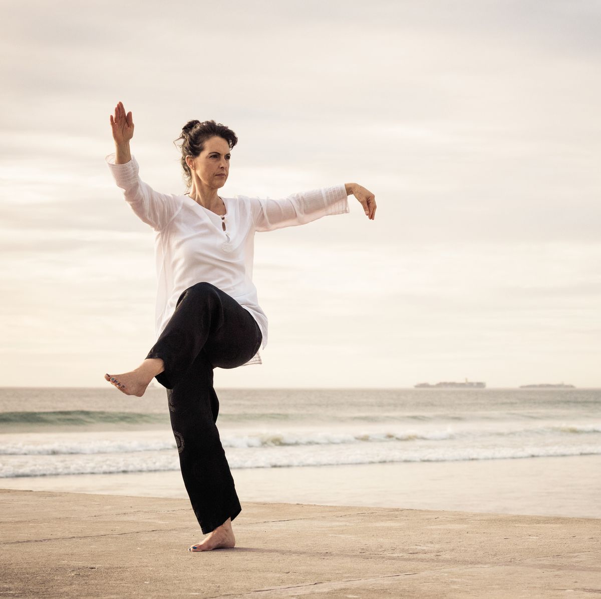woman standing poised practicing wu tai chi on the end of a concrete pier sunset behind