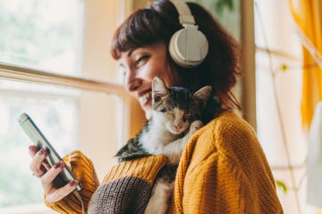 woman in a yellow sweater and headphones holding her phone and a cat