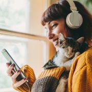 woman in a yellow sweater and headphones holding her phone and a cat