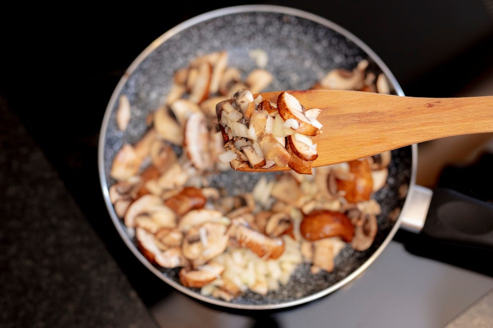 woman stirring sliced brown mushrooms in frying pan