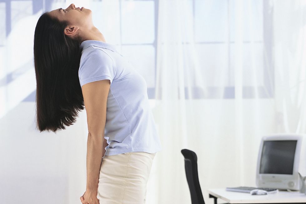 morning stretches – woman standing beside her desk doing chest opener stretch