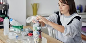 ecobricks woman stuffing soft waste plastics into large plastic bottle to make an ecobrick for use as a  building block